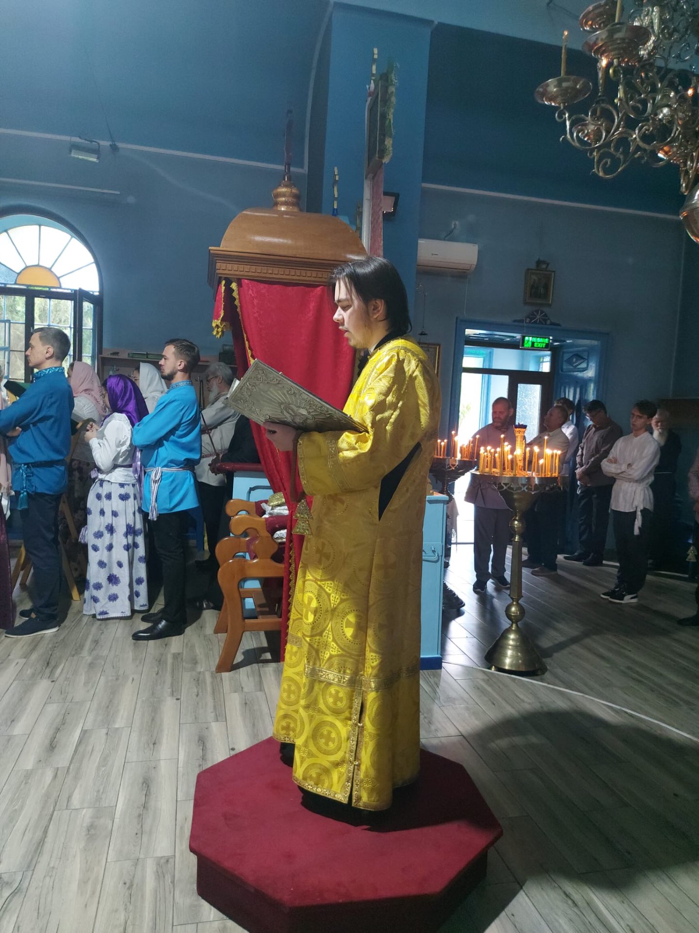 Diacon citind Apostolul în mijlocul bisericii, înconjurat de credincioși